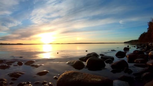 Beautiful sunset or sunrise with calm water movement at rocky lake shore. Video taken in Pulkkilanha