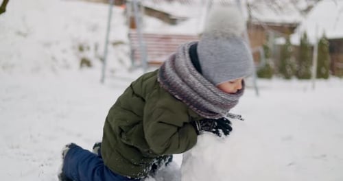 Child Building Snowball in Winter Garden