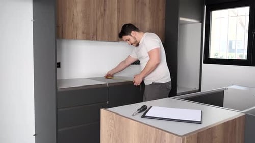 Young hispanic man using measuring tape before placing countertops on kitchen.