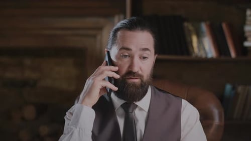 Bearded Businessman in a Suit Having Serious Phone Discussion About a Deal in Modern Office