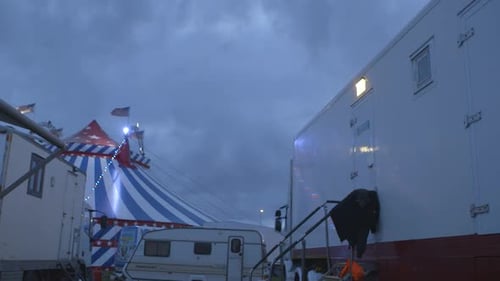 Circus performers caravan in the foreground with circus tent at the back at night time.