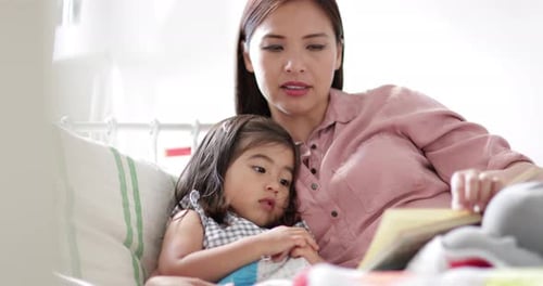 Mother reads book to young child in bed