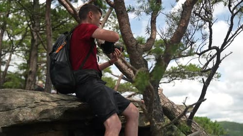 Young outdoors man photographer picks up his camera to take a landscape photo in the forest