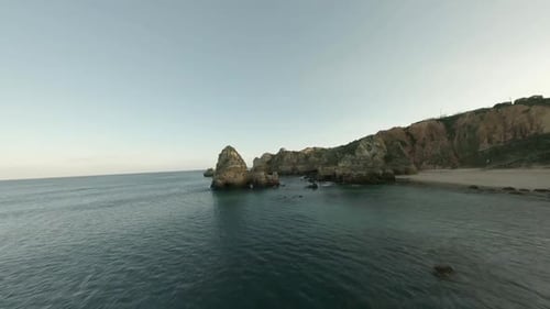 Aerial flies fast over calm ocean coastal rocks at southern Portugal