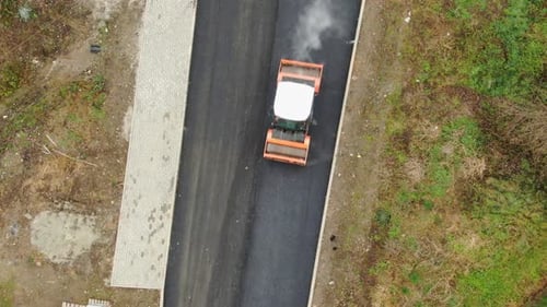 Heavy roller on road construction site pressing new asphalt layer aerial top down
