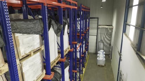 Inside a warehouse: many shelves laden with neatly stacked pallets. Camera moving from one side to a