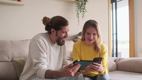 Happy Couple Using Tablet and Phone at Home