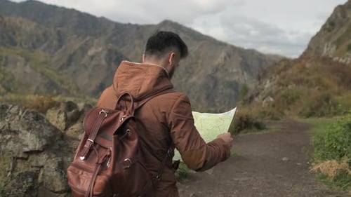 Man with Backpack Looks at Map in Mountains
