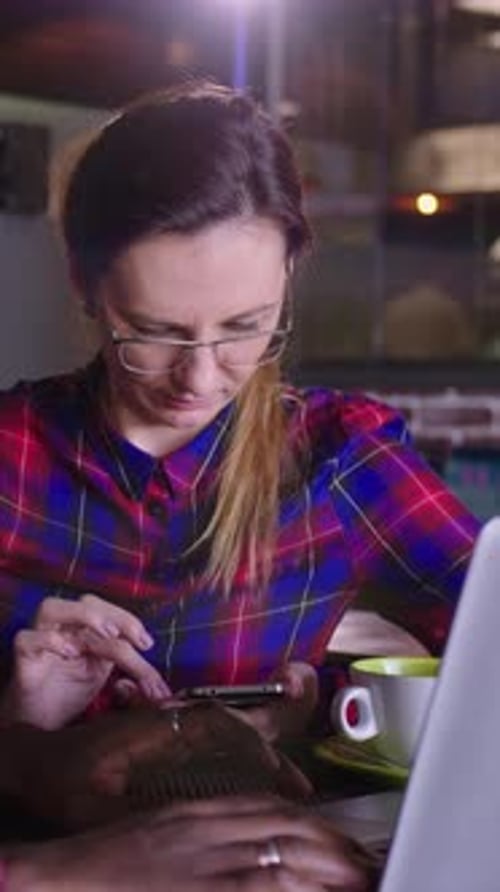 Focused Woman in Plaid Shirt Working on Laptop with Coffee Cup in Modern Cafe Environment