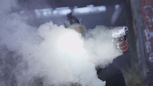 Un homme masqué tire à travers une épaisse fumée avec un pistolet à lampe de poche