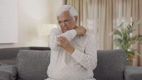 Senior Man Rubbing Sore Elbow on Couch