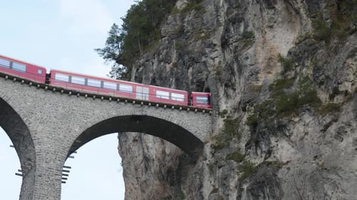 Train panoramique suisse rouge traditionnel passant sur un pont en pierre et traversant un tunnel de montagne à Lan