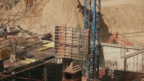 Une grue de construction soulève un grand panneau de coffrage sur le chantier