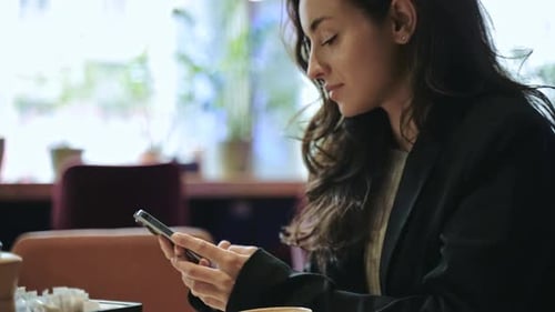 Beautiful Caucasian Girl Sitting Inside a Good Cafe Drinking Coffee Smiling and Typing on Her
