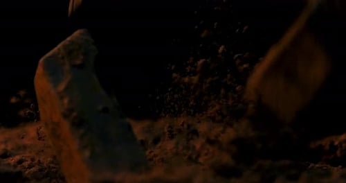 Slow motion static shot of falling chocolate pieces in cocoa while the ground rotates against a blac