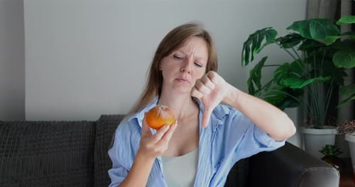 Young Woman Holding Moldy Orange Gives Thumbs Down