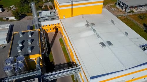 Yellow and white buildings of the industrial plant. Silver pipes among the premises of the factory.