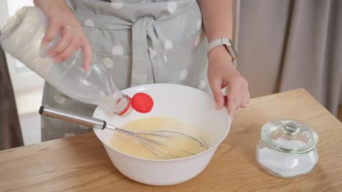 Frau gießt Milch in eine Schüssel mit Eiern und verquirlt die Omelettmischung