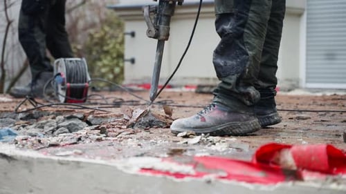 A worker at a construction site demolishing asphalt or concrete pavement with a pneumatic jackhammer