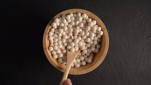 Organic tapioca pearls in wooden bamboo bowl on black table top view.