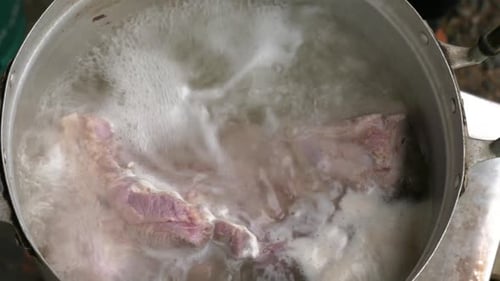 Pork belly is boiled in steaming hot water in top down handheld view