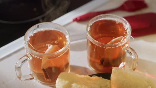 Zwei dampfende Glasbecher mit Bernsteintee und Teebeuteln neben frischen Pfannkuchen