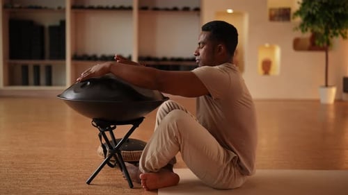 Relaxed African Man Playing Traditional Ethnic Music Using Glucophone Sitting on Floor in Lotus Pose