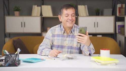 Man Using Phone and Counting Money at Desk