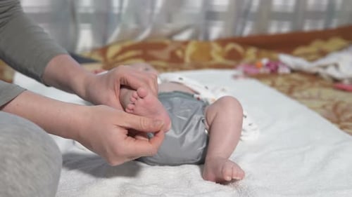 Woman Gently Massages Infant's Foot on Bed