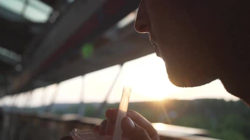A young man is drinking bubble tea, while he sits on a sunny terrace.