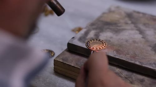 Nahaufnahme eines Goldschmieds beim Löten eines Goldschmuckstücks
