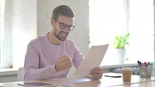 Excited Young Man Reading Documents and Cheering in Office