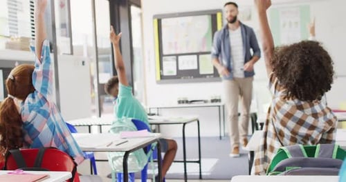 Diverse male teacher and happy schoolchildren at desk in school classroom