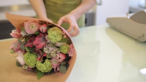 Young florist man wrapping beautiful flower bouquet for customer in flower shop