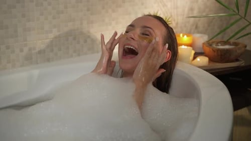 A Woman is Relaxing in a Bubble Bath with Eye Patches Enjoying a Spa Treatment The Bathroom is It