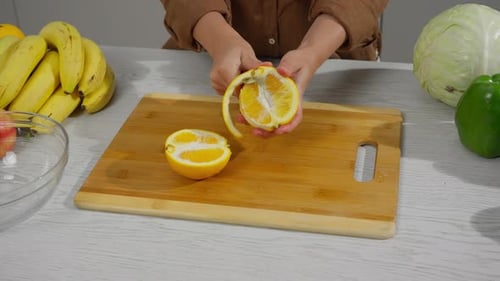 Hands Peeling Orange on Wooden Cutting Board
