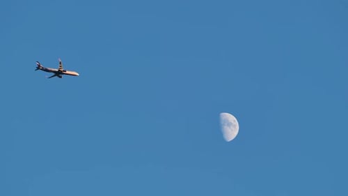 An Airplane Takes Off Against the Moon and Blue Sky