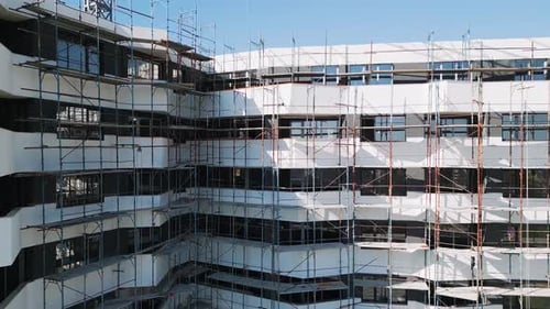 Baufortschritt eines modernen Wohnhauses mit Gerüst in einem belebten Stadtgebiet