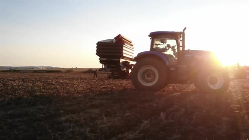 Tractor with Trailer Driving Through Farm Field at Sunset