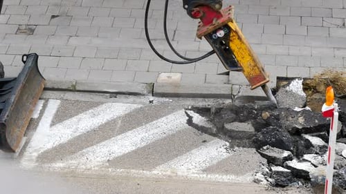 Excavator hydraulic hammer breaking asphalt road surface on reconstruction site