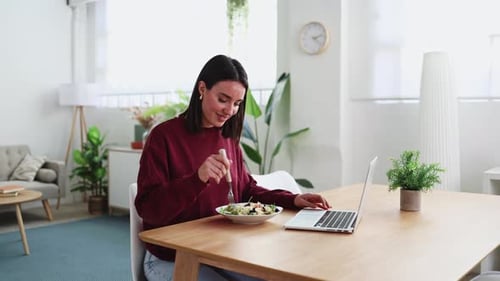 Woman Eating Salad and Typing on Laptop at Home