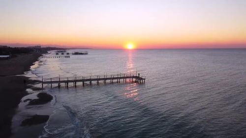 Man standing on an old pier, sunrise on the horizon, wavy sea aerial shot