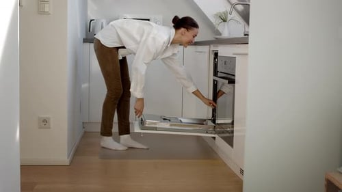 Happy Woman Coming to Kitchen and Opening Dishwashing Machine Putting Dirty Plates Into It and Going