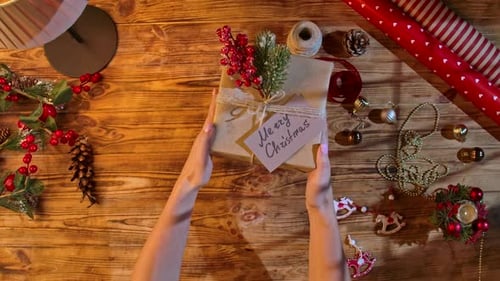 Hands Passing Christmas Present Overhead on Wooden Table