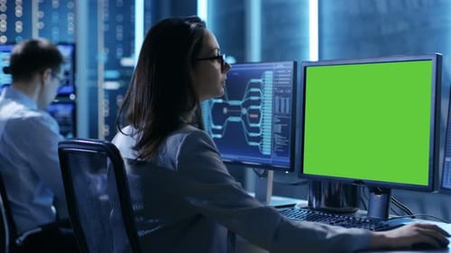 Controlador/operador femenino trabajando en su estación de trabajo con varias pantallas (maqueta de pantalla verde)