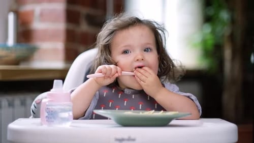 Toddler Eating Food at Table with Spoon