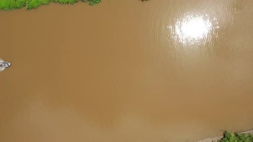 Top down aerial view of people riding boat in murky Indonesian jungle river