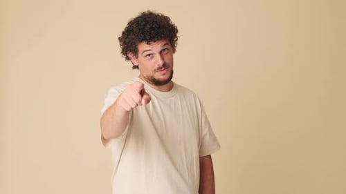 Smiling man pointing finger at camera in studio on beige background