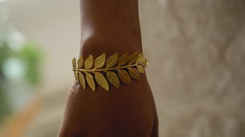 Beautiful bride trying on a golden leaf like bracelet in her wedding dress with beautiful bokeh in t