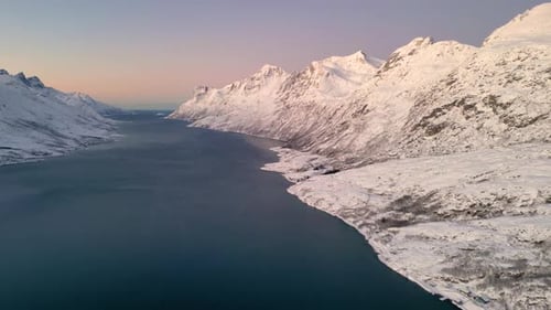 Serene snowy fjord during sunset with mountains reflecting on calm waters